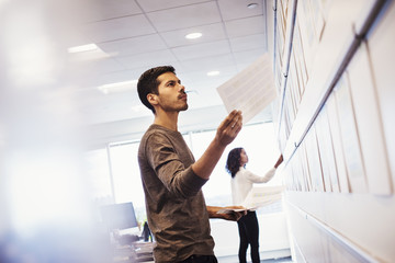 A woman and a man standing in an office adding pieces of paper to a display on a wall.