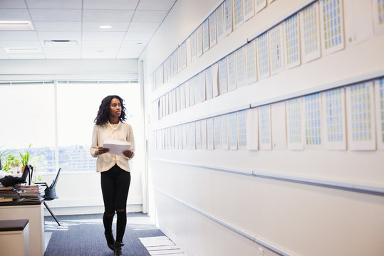 A woman standing in an office looking at a display holding pieces of paper.