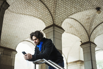 A man checking his smart phone and leaning on a stair railing. 