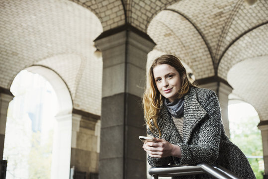 A woman with long hair looking at her smart phone, under an archway. 