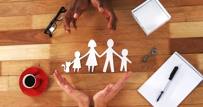 Close-up of cutout paper chain family with the protection of hands on table at home 4k
