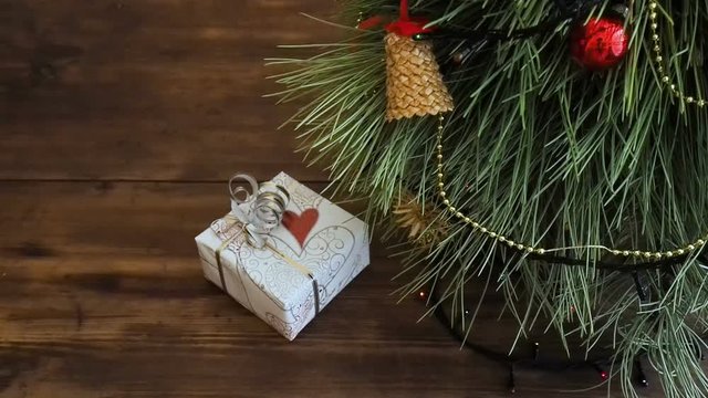 The man puts gift boxes under the Christmas tree. Fir stand on the wooden table, decorated glowing garland and Christmas toys. Boxes with gift wrapped in brown and colored paper and tied with twine.