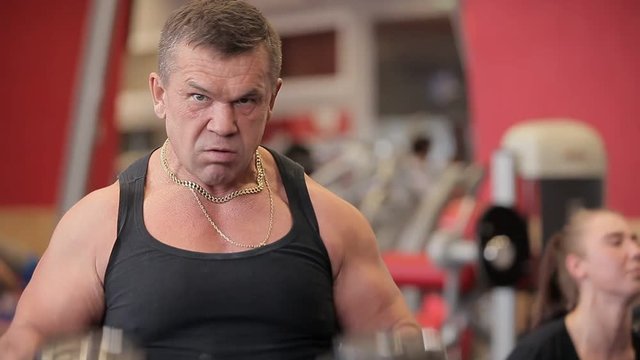 Dumbbells in the gym - muscle training. The man lifts dumbbells in the gym. The Nakacheny big man trains with dumbbells. The trainer in the gym