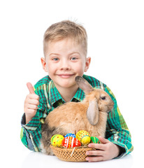 Happy boy with easter eggs embracing rabbit and showing thumbs up. isolated on white 