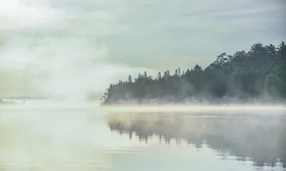 Foto op Canvas Mist en nevel stijgen overal op en omhullen gedeeltelijk een loofbos in Oost-Ontario aan het water aan een oever van het meer. © valleyboi63