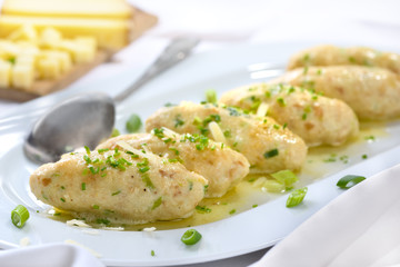 Deftige Südtiroler Kasnocken mit gebräunter Butter und Parmesen auf weißer Platte serviert -...