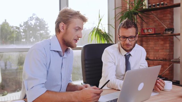 Male office worker in blue shirt explaining prokect at laptop to his Caucasian boss in glasses anf white shirt with tie in slowmotion