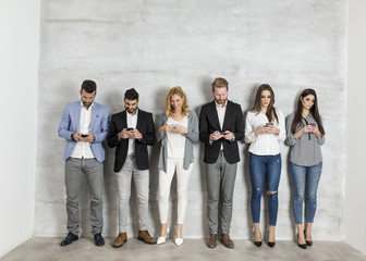 Obraz premium Young business people with mobile phone standing by the wall