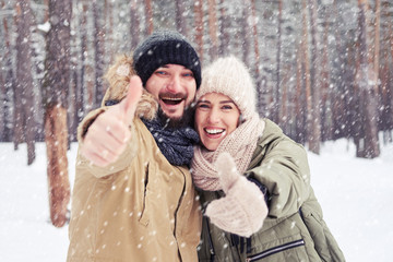 Merry couple gesturing and hugging on a cold winter snowy day