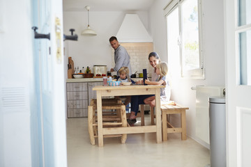 Fototapeta premium Kids at kitchen table with mum, dad cooks, view from doorway