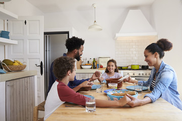 Family hold hands around the kitchen table before their meal