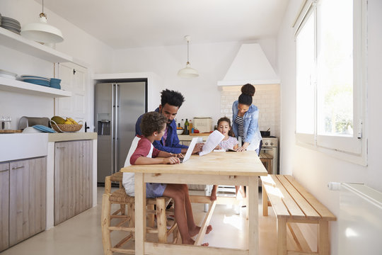 Mum and dad help their kids with homework at kitchen table