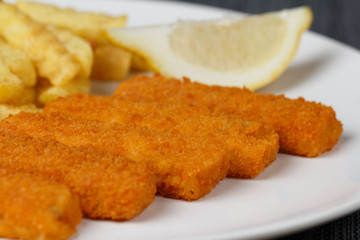 Fish fingers sticks with lemon on white plate, closeup, low focus