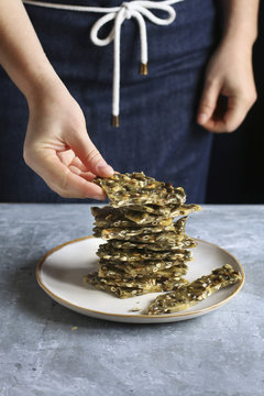 Female hand staking pieces of pumpkin seed brittle on a plate