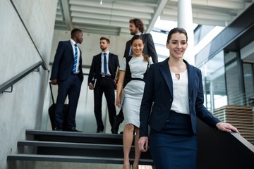 Confident businesswoman with colleagues climbing down the stairs