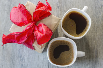 A gift with red bow and two cups of coffee on gray wooden background