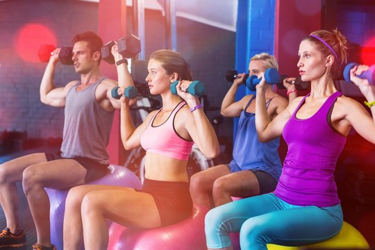 Friends holding dumbbells while sitting on fitness ball 
