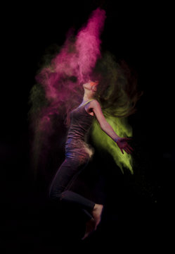 Studio photo of a young girl who is jumping and throwing powder paint. She turned the wings of yellow paint and a trace of pink paint left by the hair resembles a flame a fire-breathing dragon.