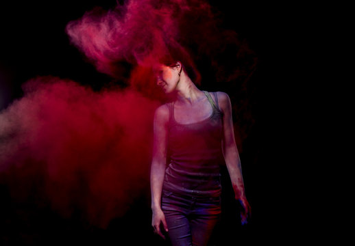 Girl in a black shirt and black jeans in the studio. She made a cloud of red powder paint with the help of her long dark hair.
