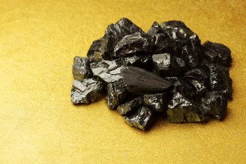 Raw coal nuggets on golden textured background