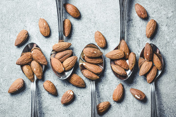 Almonds on five silver spoons located on gray grunge kitchen table surface.