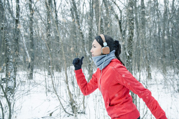 Running sport woman. Female runner jogging in cold winter forest wearing warm sporty running clothing and gloves headphones. Beautiful fit  female fitness model.