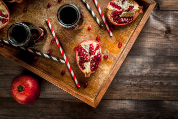Homemade pomegranate juice in bottles in a wooden tray, with straws and fresh whole and sliced pomegranates. top view, copy space