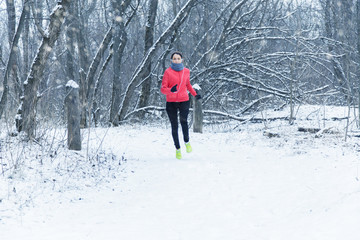 Running sport woman. Female runner jogging in cold winter forest wearing warm sporty running clothing and gloves headphones. Beautiful fit  female fitness model.