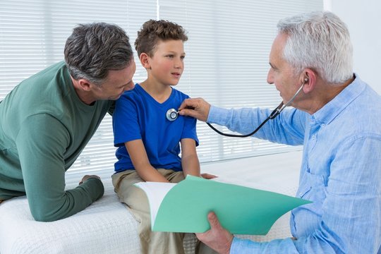 Father looking at son while being examined by doctor