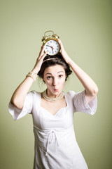 Joyful beautiful woman holding up alarm clock over light background. Portrait