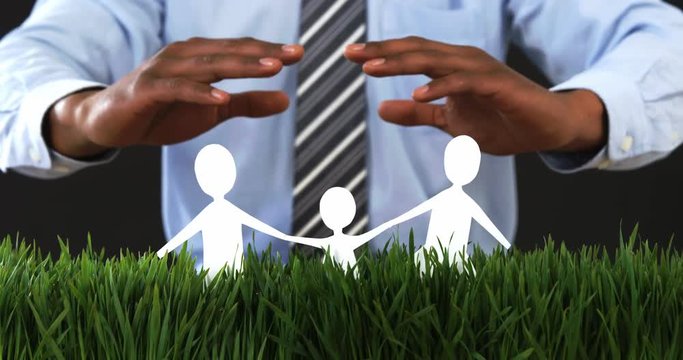Businessman with cutout paper chain family with the protection of hands on grass in office 4k