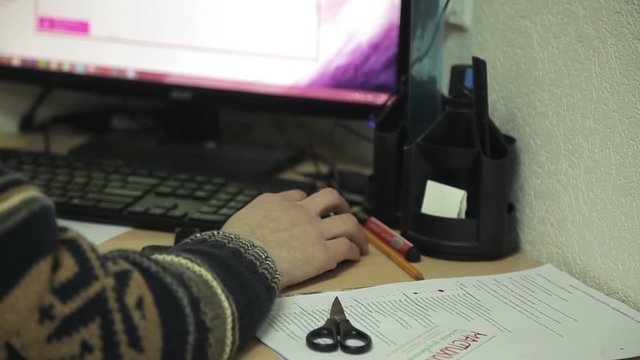 Office worker in a sweater at the table working on the computer, move the mouse cursor
