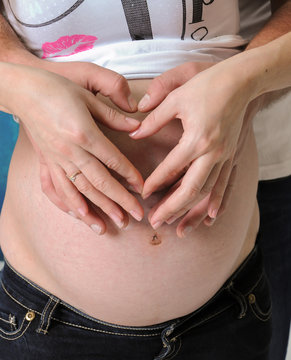 Taking care of your body. The concept of a pregnancy diet. Female hands forming heart shape on belly.
