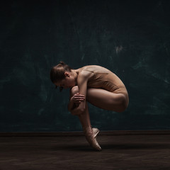 young beautiful ballet dancer in beige swimsuit posing on pointes over dark grunge background