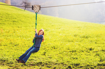 Cute little girl playing on a chain swing, having fun in a park on a nice sunny day in spring
