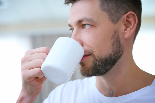 Handsome young man drinking coffee at home, closeup