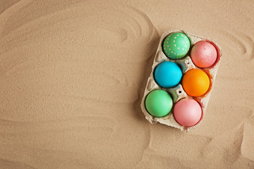 Colorful Easter eggs in carton box on sand