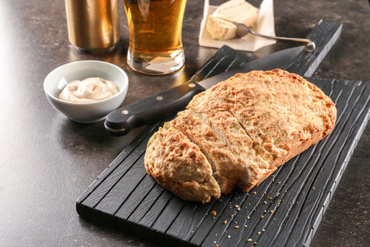 Board with tasty loaf of beer bread on table