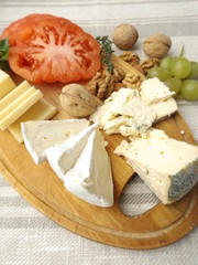 Cheeseboard. Three kinds of cheese, tomato varieties Monte Rosa, and nuts on a wooden board.