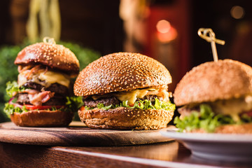 Three juicy tasty burger on the white plate on a dark background