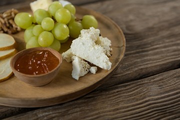 Cheese with grapes and sauce on wooden plate