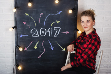 A beautiful young woman in a red shirt writing on blackboard motivational text 2017 and arrows (direction)