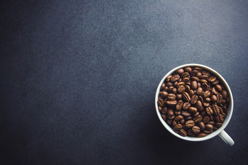 White coffee cup filled with coffee seeds on black surface background.