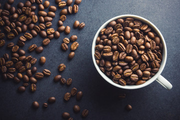 White coffee cup filled with coffee seeds on black surface background.
