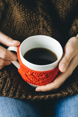 Red Knitted woolen cup with heart pattern in female hands. Hands holding a cozy Mug in red knitted mitten with hot cocoa, tea or coffee. Valentines day concept