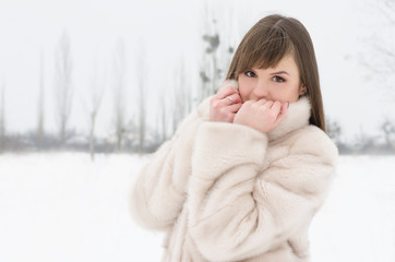 Beauty joyful teenage model girl having fun in winter park. Beautiful young woman in a fur coat...