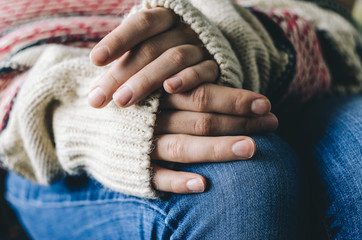 Fototapeta na wymiar Girl's hands in casual wool sweater on her knees on denim jeans. Warmth and comfort concept. Winter mood.