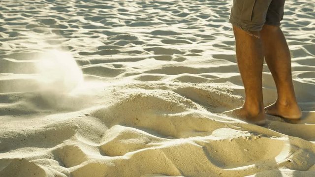Legs of tanned man in khaki shorts sieving sand with feet. Barefoot human playing in desert. Senseless act and loneliness concept. Close-up. Side view.