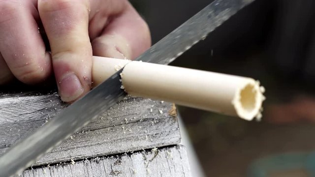 Close up shot of a person cutting a PVC water pipe with a hacksaw to do some home improvements or plumbing repairs.