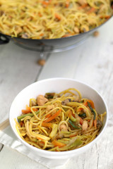 Noodles with chicken and various vegetables, prepared in wok. Served on white rustic table. Selective focus. 
